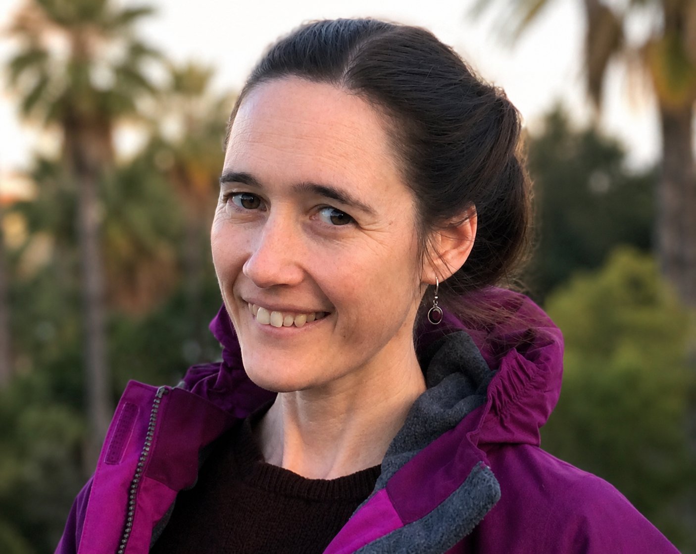 Portrait of Aline Gram Lewis, a woman with dark hair pulled back, smiling gently and looking just past the camera.
